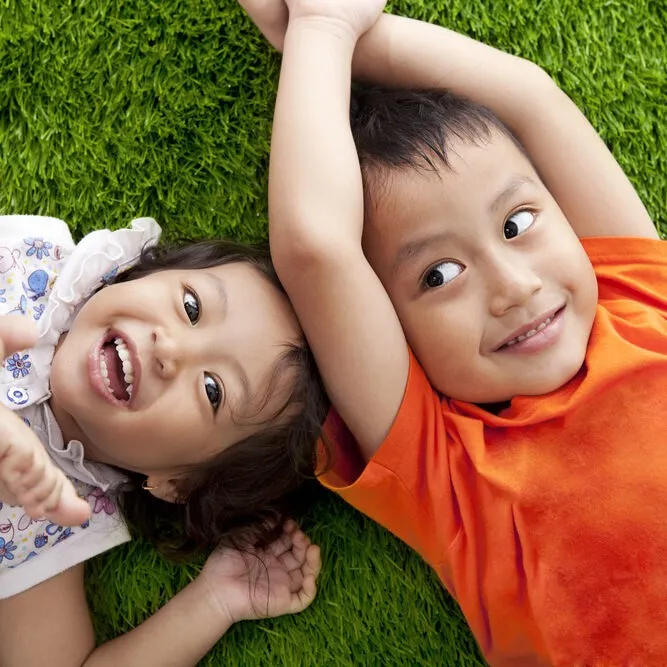 Cute,Happy,Asian,Siblings,Lying,On,The,Green,Grass,Shot